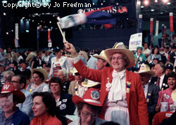an older woman stands and waves a flag in a seated crowd