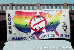 a huge sign hanging from a bridge reading ACORN alliance for justice with a drawing of Reagan with a red slash through it and a rainbow in the shape of the USA