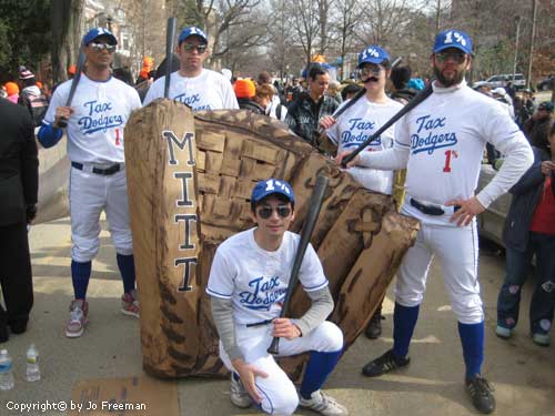 protestors stand near a huge baseball Mitt and wear baseball uniforms with the words Tax Dodgers and 1 percent on them