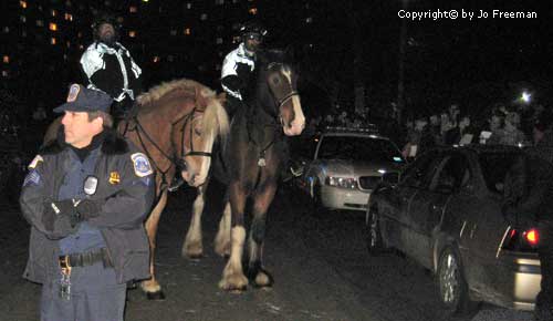 protestors stand near two police on horses and a third policeman standing in the foregraound