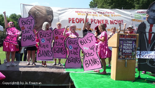 Protestors stand on a stage wearing hourglass figure shaped signs reading Bust up the Banks