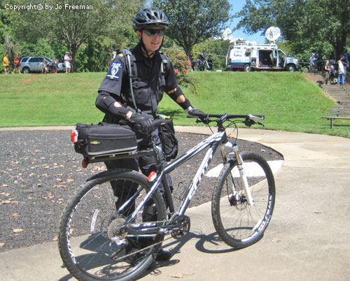 a smiling cop stands near her bike and wears head to tow protective gear