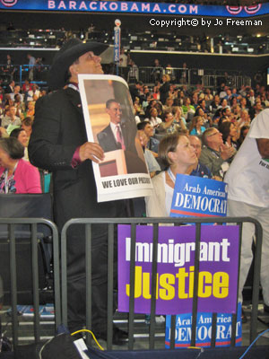 A man stands near an immigrant justice poster and holds a sign reading we love our president