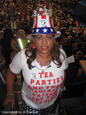 A woman wears a stars and stripes top hat and a shirt reading Tea Parties and their mangina friends are for little girls