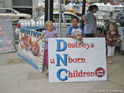 children prop up a graphic poster of an aborted fetus and another linking the DNC to the destruction of unborn children