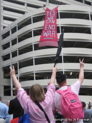 two code pink people stand in front of a sign reading Yes We Can End War