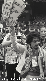 An older female deligate wears a National Education Association sash and a large ERA sign