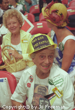 An elderly female deligate wears a construction hat with the words pro god pro family pro ERA on it.  She also wears a shirt with apicture of herself wearing the hat. in the background a woman wearing a hat with crabs on it sits next to a smiling woman holding an easter basket.