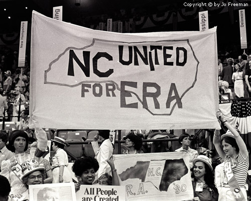 Many women hold a gigantic fabric sign reading NC united for ERA