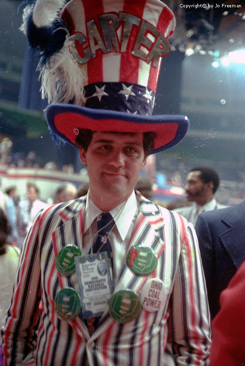 Male deligate wears elaborate hat and striped suit.  The hat reads Carter