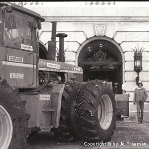 A tractor and farmer stand near an opulent building
