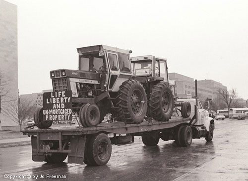 A truck carries two tractors, onw with a sign reading Life Liberty and Un-Mortgaged Property