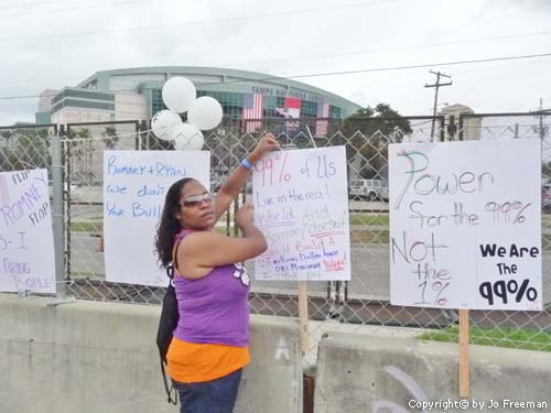A protestor stands by posters against the fence on the other side of the convention center