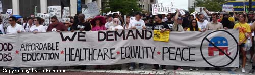 many protestors hold up a sign reading we demand equality healthcare affordable education and peace