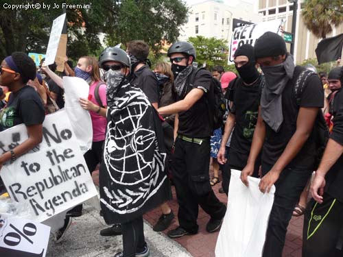 demonstrators wearing all black, with helmets and covered faces