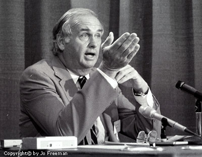 The senator speaking into several microphones from behind a desk