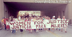 a large group of protestors carry one wide banner reading Women for Justice and the same message in Spanish.