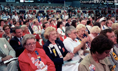 a row of middle aged women sit among many male audience members